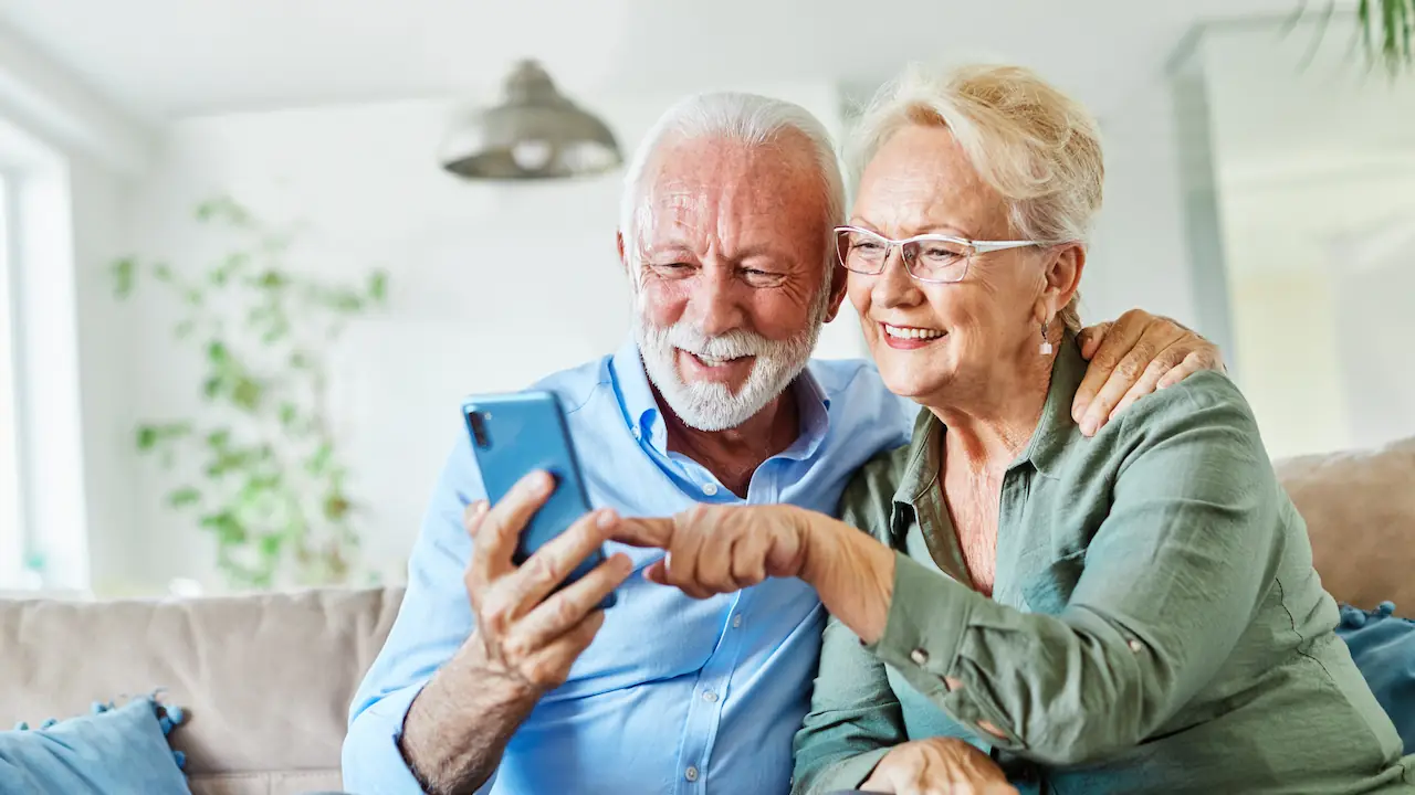 elderly couple smiling while looking at photos on their cell phone